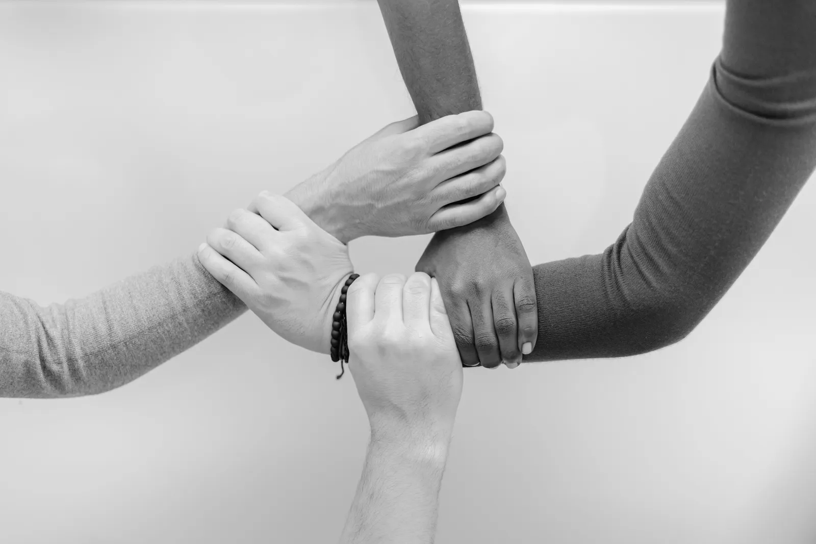 Four hands holding each other's wrists in a ring